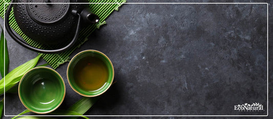 Green tea in cups beside a cast iron teapot on slate