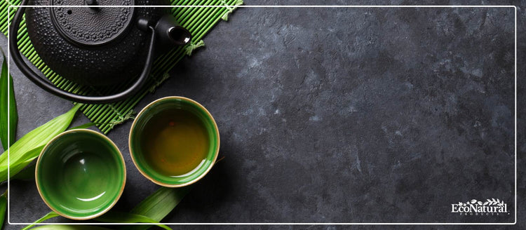 Green tea in cups beside a cast iron teapot on slate